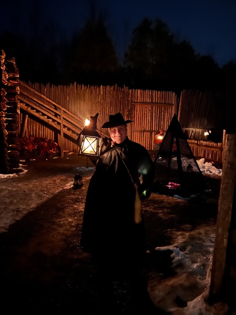 Blake, a historical interpreter in jesuit garb, holds up a lantern at night