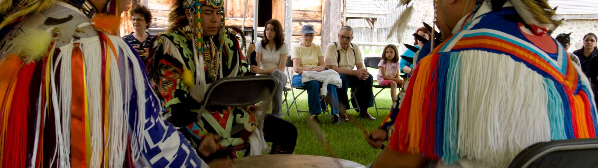 Quatres hommes autochtones en habits cérémoniaux, à jouer un gros tambour en chantant