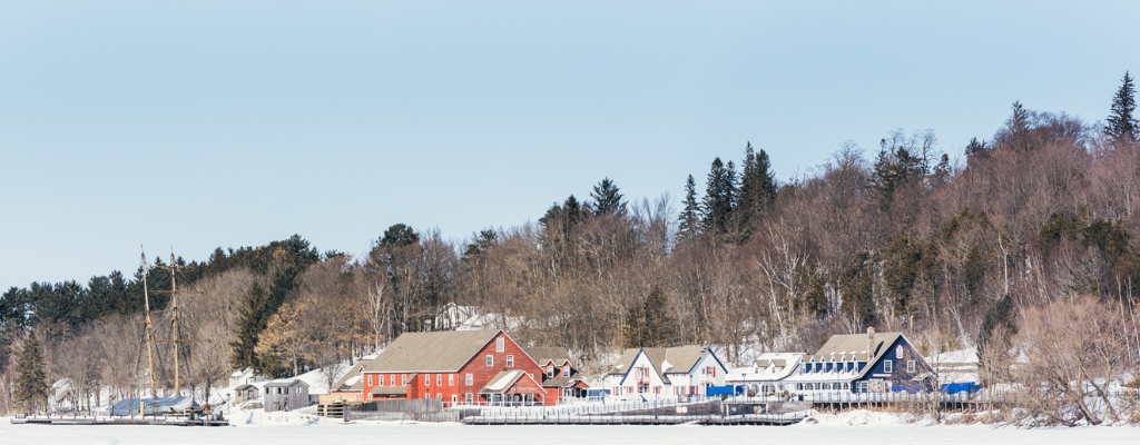 The shoreline of Discovery Harbour in winter with the Kings' Wharf Theatre, the buildings and the ship