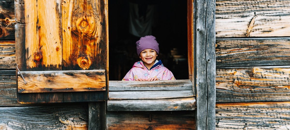 Une petite fille souriante regardant de l'intérieur d'un immeuble à Sainte-Marie - les volets sont grands ouverts