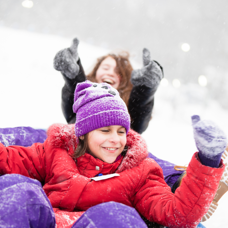 Two girls in winter clothes are smiling after coming down the snow tube hill