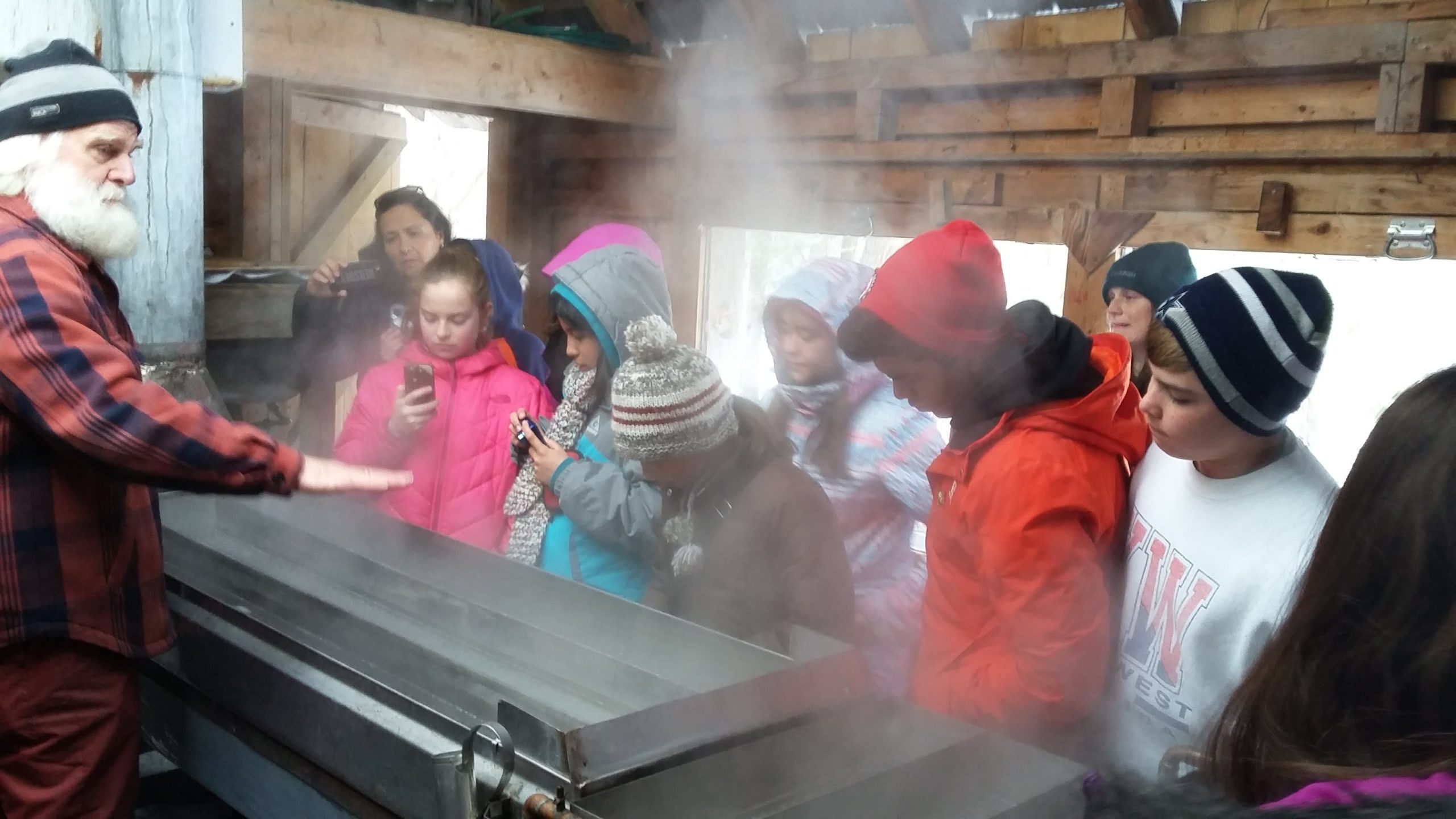 A volunteer shows guests how to work a syrup evaporator
