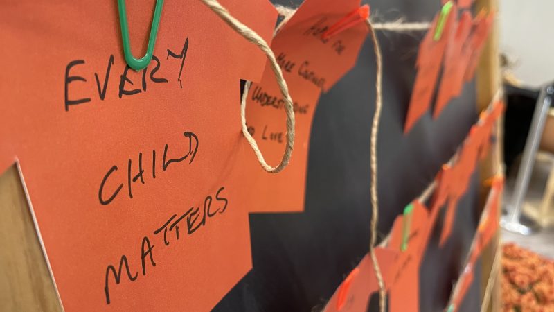 string of small orange cardstock t-shirts with writing on them to commemorate national day for truth and reconciliation. First card reads 