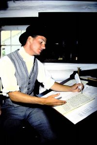man in top hat writing with quill pen inside the Office of the Clerk-in-Charge
