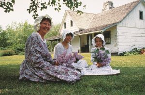 three women in historical dresses sitting on the lawn outside of Keating House