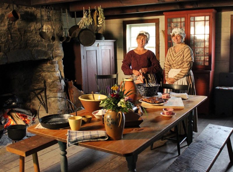 two women in historic clothing standing behind a historical diner setting 