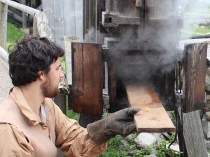 man pulling a steaming wooden plank from Steam Kiln