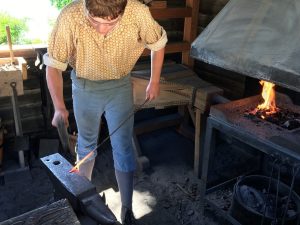 man hammering heated metal rod inside the Blacksmith Shop